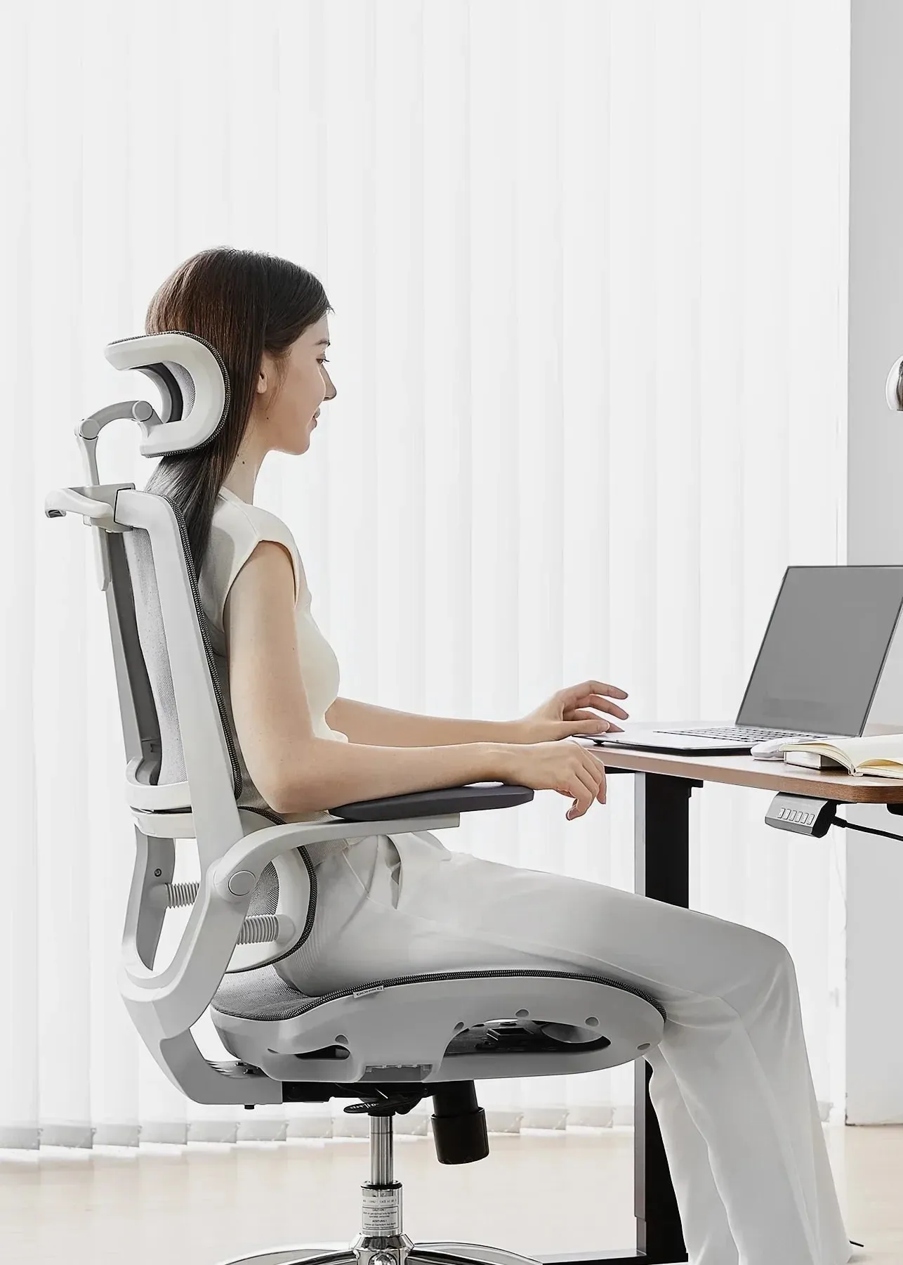 Femme travaillant sur une chaise ergonomique Sihoo blanche, face à un bureau réglable