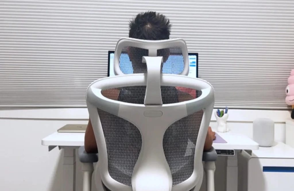 Homme assis face à son bureau sur une chaise de bureau ergonomique avec appui-tête, adoptant une posture droite et équilibrée pour réduire les tensions cervicales.
