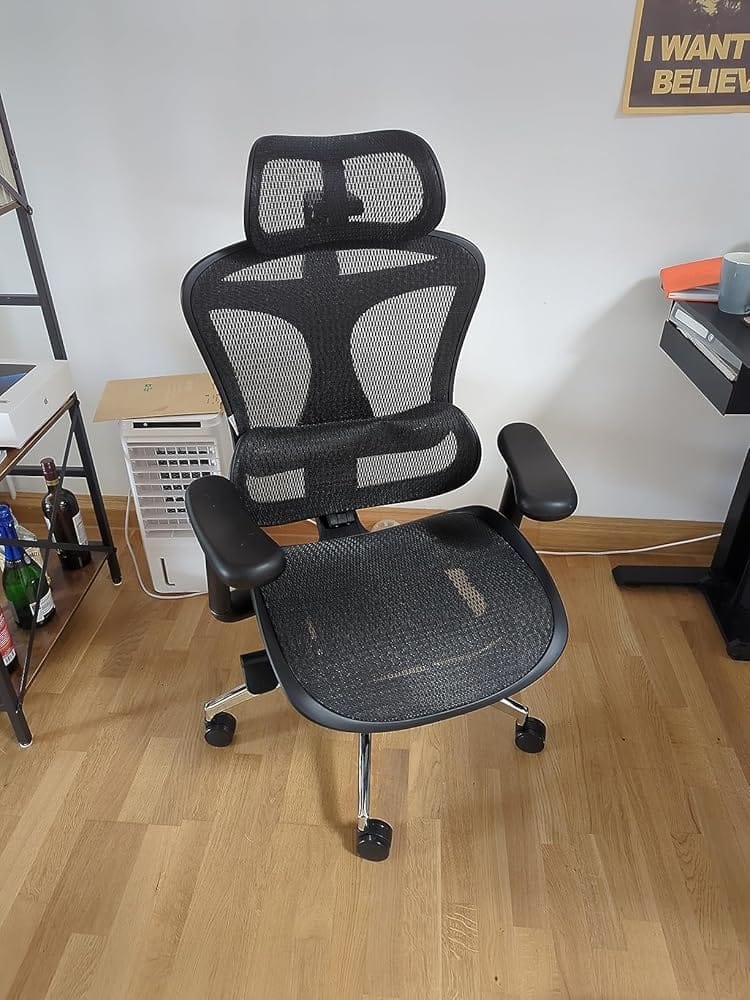 Chaise de bureau ergonomique noire en filet usée, avec accoudoirs réglables et appui-tête, montrant des signes d’usure sur l’assise.